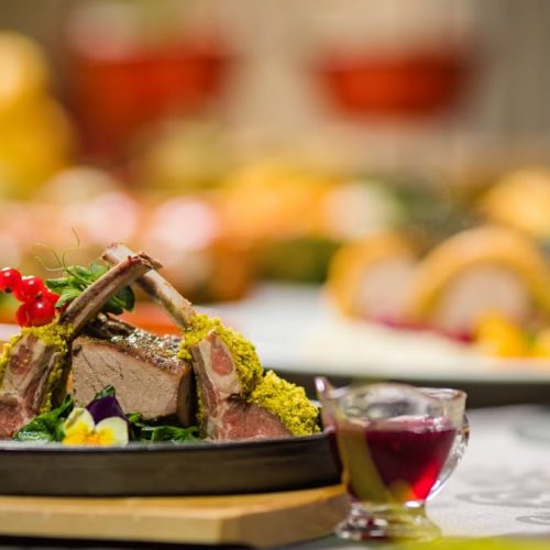 Close-up of a gourmet lamb rack with herbs, served with sauce, on a rustic table setting. Perfect for culinary themes.