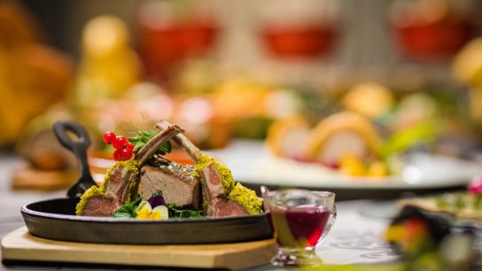 Close-up of a gourmet lamb rack with herbs, served with sauce, on a rustic table setting. Perfect for culinary themes.