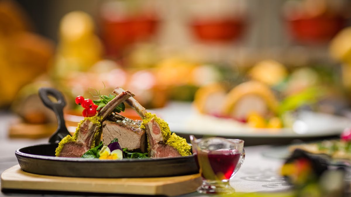 Close-up of a gourmet lamb rack with herbs, served with sauce, on a rustic table setting. Perfect for culinary themes.